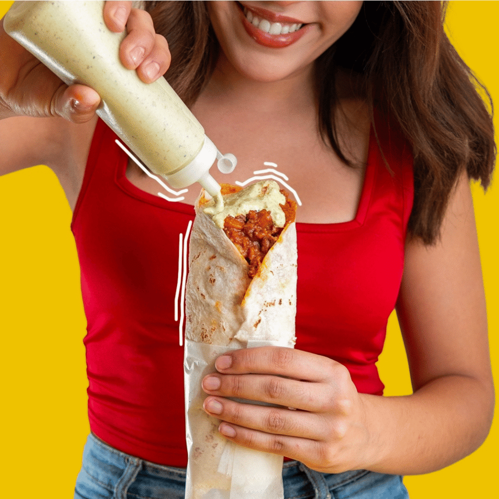 Mujer sonriente sosteniendo su burrita de chcicharrón mientras le echa salsa guacamole